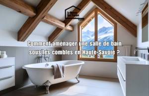 Salle de bain aménagée sous les combles avec poutres apparentes, baignoire îlot et vue sur les montagnes en Haute-Savoie – conseils d’aménagement.
