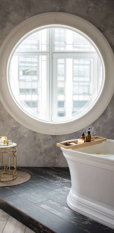 Une salle de bain avec une fenêtre ronde une baignoire et des murs couverts de tadelakt gris 