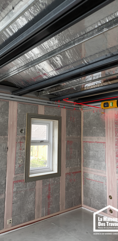 Détail technique d'un chantier d'extension avec pose d'isolation en laine de verre et rails métalliques.