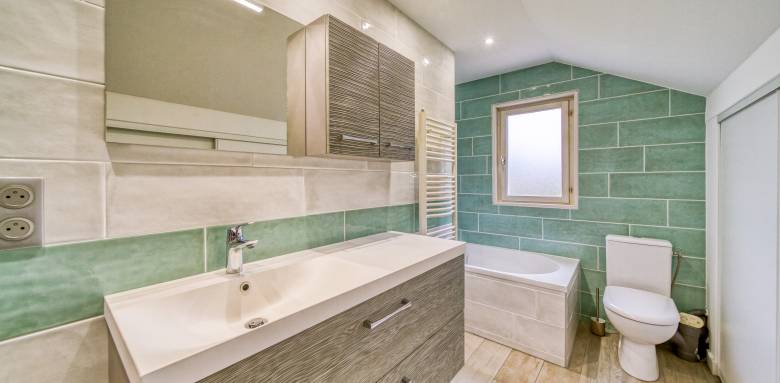 Dans la salle de bain, un éclairage blanc au plafond avec une source secondaire au dessus du lavabo