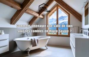 Salle de bain aménagée sous les combles avec poutres apparentes, baignoire îlot et vue sur les montagnes en Haute-Savoie – conseils d’aménagement.