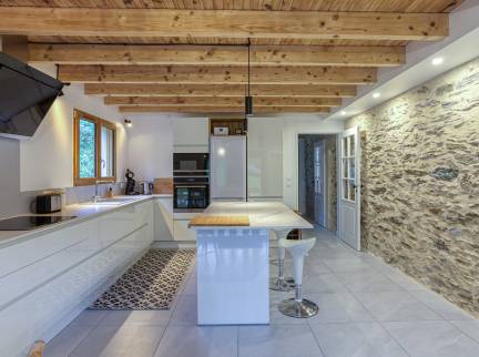 La cuisine tout en blanc, avec poutre apparente et mur en pierre