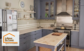 Cuisine rénovée au style campagne chic avec meubles bleu-gris, crédence claire et îlot central en bois patiné – un projet réalisé par La Maison Des Travaux Quimper.