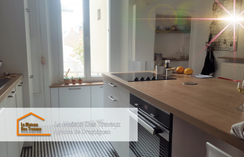 Vue d’ensemble de la cuisine rénovée, avec des éléments fonctionnels et un sol en damier qui ajoute du caractère à la pièce.