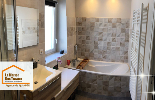 Salle de bain rénovée avec carrelage mural texturé, baignoire d’angle et meuble vasque suspendu.