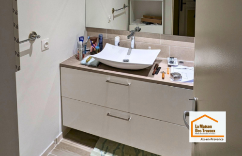 Meuble vasque contemporain avec rangements, grand miroir et revêtement effet pierre dans une salle de bain entièrement rénovée à Aix-en-Provence.