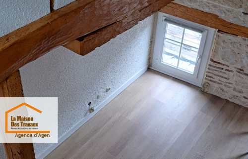 Zoom sur le charme authentique conservé dans cette chambre rénovée à Agen : poutres apparentes, mur en pierre et sol PVC bois clair posé avec soin.