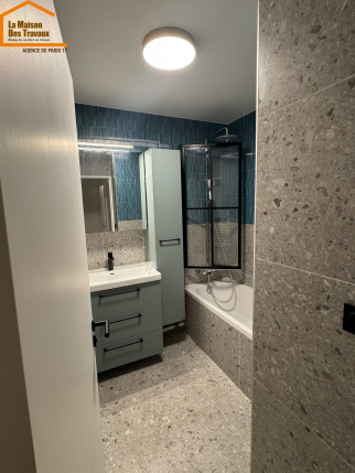 Rénovation de salle de bain avec baignoire, paroi vitrée noire et meuble vasque bleu