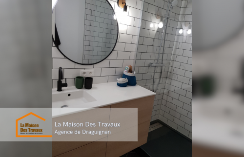 Meuble vasque suspendu en bois clair et miroir rond, ajoutant du caractère et de la praticité à cette petite salle de bain d’appartement.