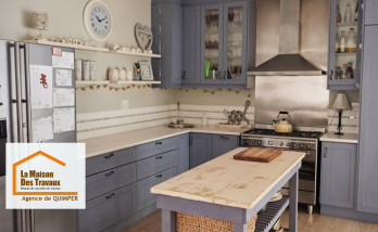 Cuisine rénovée au style campagne chic avec meubles bleu-gris, crédence claire et îlot central en bois patiné – un projet réalisé par La Maison Des Travaux Quimper.