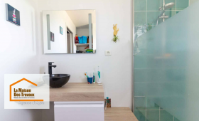 Vue d’ensemble lumineuse d’une salle de bain moderne comprenant une douche à l’italienne avec paroi vitrée et des carreaux vert émeraude. Le meuble suspendu en bois clair, surmonté d’une vasque noire design, apporte une touche d’élégance et de modernité.