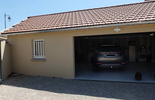 Réalisation d'un garage double avec portail coulissant, attenant à une maison existante, commune de l'ouest de Lyon : cour gravillonnée et porte sectionnelle motorisée