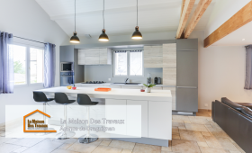 Une cuisine moderne avec un îlot central spacieux et élégant, idéal pour les repas en famille. Les suspensions noires apportent une touche de design, contrastant joliment avec les meubles en bois clair et gris.