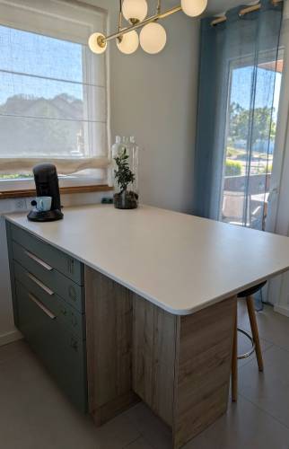 Îlot central sur mesure dans une cuisine rénovée à Voiron, avec plan de travail blanc, rangements et coin repas.