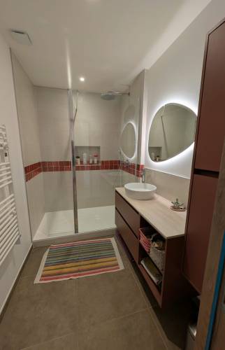 Salle de bain entièrement rénovée à Voiron avec grande douche vitrée, meuble vasque et miroir rétroéclairé.