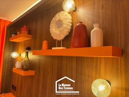 Détail d'une niche éclairée intégrée dans une tête de lit sur mesure en bois foncé.