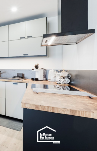 Plan de travail en bois avec plaque de cuisson intégrée, crédence noire mate et meubles hauts épurés dans une cuisine rénovée en Haute-Savoie.