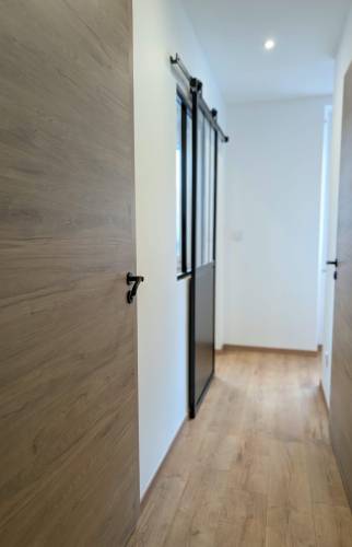 Couloir rénové à Voiron avec revêtement de sol effet bois, portes contemporaines et verrière coulissante.