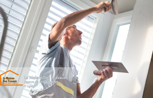 Un artisan en plein travail sur un mur, appliquant un enduit avec précision pour lisser les imperfections. 