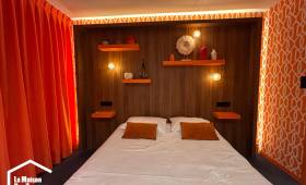 Vue d'ensemble d'une chambre parentale rénovée avec tête de lit en bois et rideaux orange.