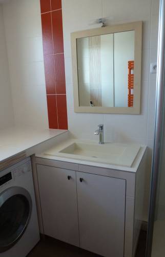 Aménagement de la salle d'eau en buanderie avec lave linge, meuble avec lavabo intégré et douche adjacente dans appartement ancien à Douarnenez (29)