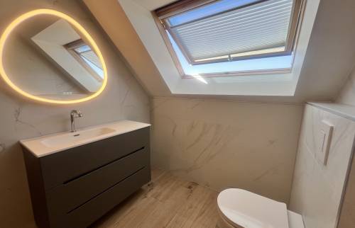 Salle de bain rénovée sous combles avec meuble vasque suspendu et miroir rétroéclairé.