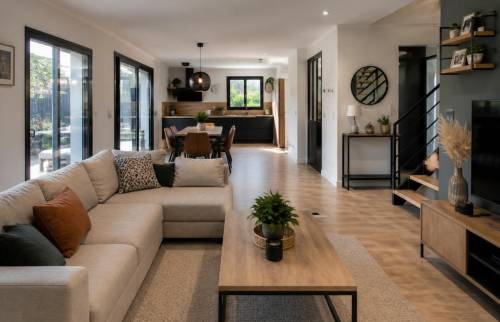 Pièce de vie contemporaine avec cuisine noire et bois ouverte sur un salon lumineux, parquet en bois et escalier bois et métal.