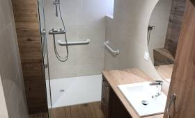 Salle de bain rénovée à Charancieu avec douche accessible, barres de maintien, meuble vasque et finitions effet bois.