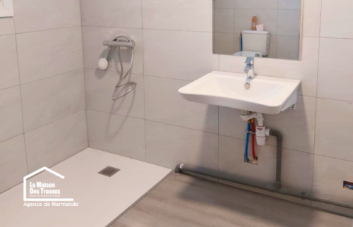 Salle de bain PMR rénovée à Castillonnès avec douche de plain-pied, lavabo suspendu et espace dégagé pour faciliter les déplacements.