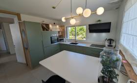 Vue d’ensemble de la cuisine contemporaine vert sauge et bois après rénovation dans une maison à Voiron.