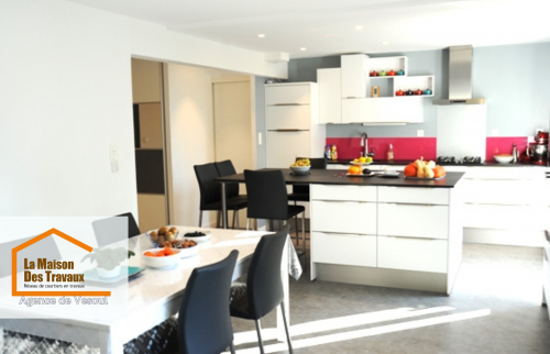 Vue ouverte sur séjour à Lure – Cuisine contemporaine avec coin repas, grandes baies vitrées et salon cosy. Rénovation moderne et épurée.