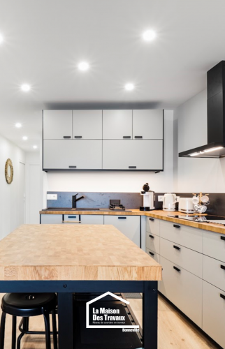 Cuisine contemporaine avec îlot central en bois massif, rangements minimalistes gris clair et hotte noire design – projet en Haute-Savoie.