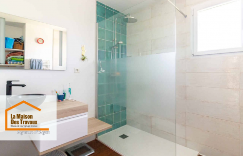 Gros plan sur la douche à l’italienne, avec des carreaux vert émeraude au design contemporain, un mitigeur et une douche de tête élégants. Une paroi vitrée épurée sépare harmonieusement la zone de douche du reste de la pièce.