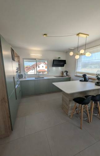 Rénovation d’une cuisine dans une maison des années 70 à Voiron, avec meubles vert sauge, plan de travail blanc et îlot central convivial.