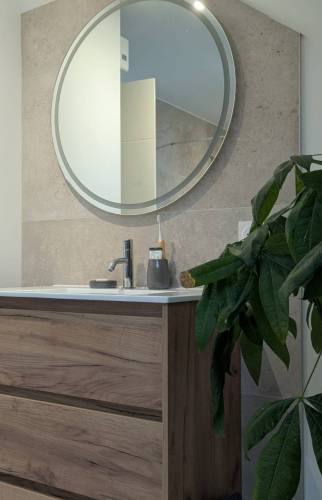 Meuble vasque en bois et miroir rond dans une salle d’eau rénovée