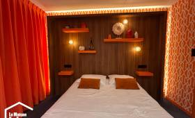 Vue d'ensemble d'une chambre parentale rénovée avec tête de lit en bois et rideaux orange.