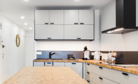 Cuisine contemporaine avec îlot central en bois massif, rangements minimalistes gris clair et hotte noire design – projet en Haute-Savoie.