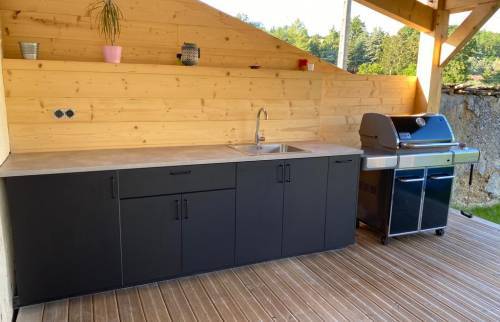 Alliance du bois et du mobilier noir pour cette cuisine d'été moderne réalisée sur une terrasse en bois à Coublevie.