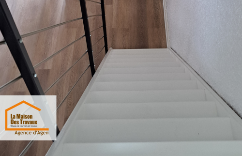 Un escalier repeint en blanc et sécurisé mène vers un espace de vie lumineux, où le sol PVC effet bois offre chaleur, confort et modernité.