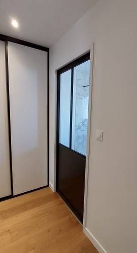 Porte coulissante de type verrière d'atelier intégrée à la cloison pour accéder à la salle de bain depuis le dressing