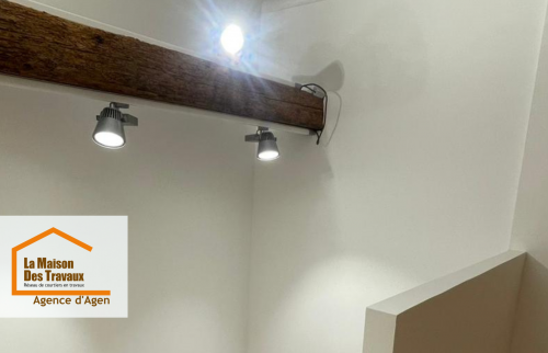 Jeu de lumière et charme de l’ancien : mise en valeur des poutres et installation de luminaires modernes pour une ambiance douce sous les toits.