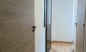 Couloir rénové à Voiron avec revêtement de sol effet bois, portes contemporaines et verrière coulissante.