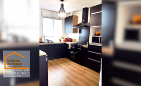 Après rénovation : Nouvelle cuisine contemporaine avec des meubles noirs et bois, un parquet stratifié chaleureux et des équipements haut de gamme.