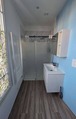 Salle de bains moderne rénovée avec meuble vasque blanc, miroir rond et douche vitrée