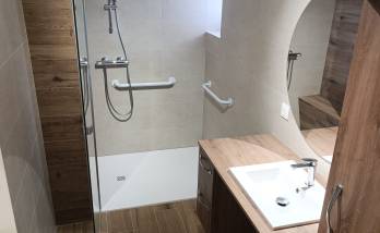 Salle de bain rénovée à Charancieu avec douche accessible, barres de maintien, meuble vasque et finitions effet bois.
