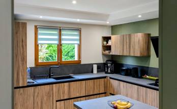 Vue d'ensemble de la cuisine, avec une belle harmonie bois, vert sauge et noir