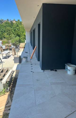 Pose d’un carrelage extérieur grand format pour la création d’une terrasse contemporaine autour d’une maison à Voiron.