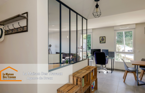 Une verrière élégante sépare l’entrée du salon, apportant une touche industrielle moderne et laissant entrer la lumière naturelle.