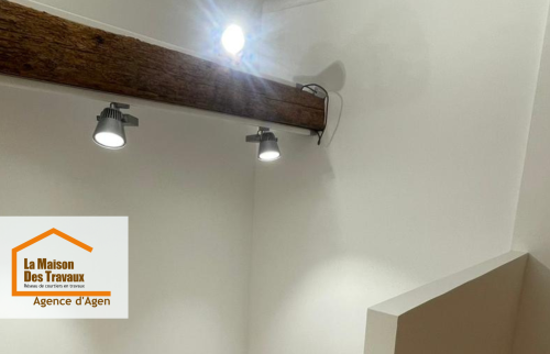 Jeu de lumière et charme de l’ancien : mise en valeur des poutres et installation de luminaires modernes pour une ambiance douce sous les toits.