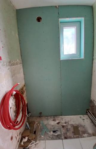 Chantier en cours à Courrières : isolation du mur du fond avec des plaques hydrofuges et préparation des réseaux de plomberie avant la pose du carrelage